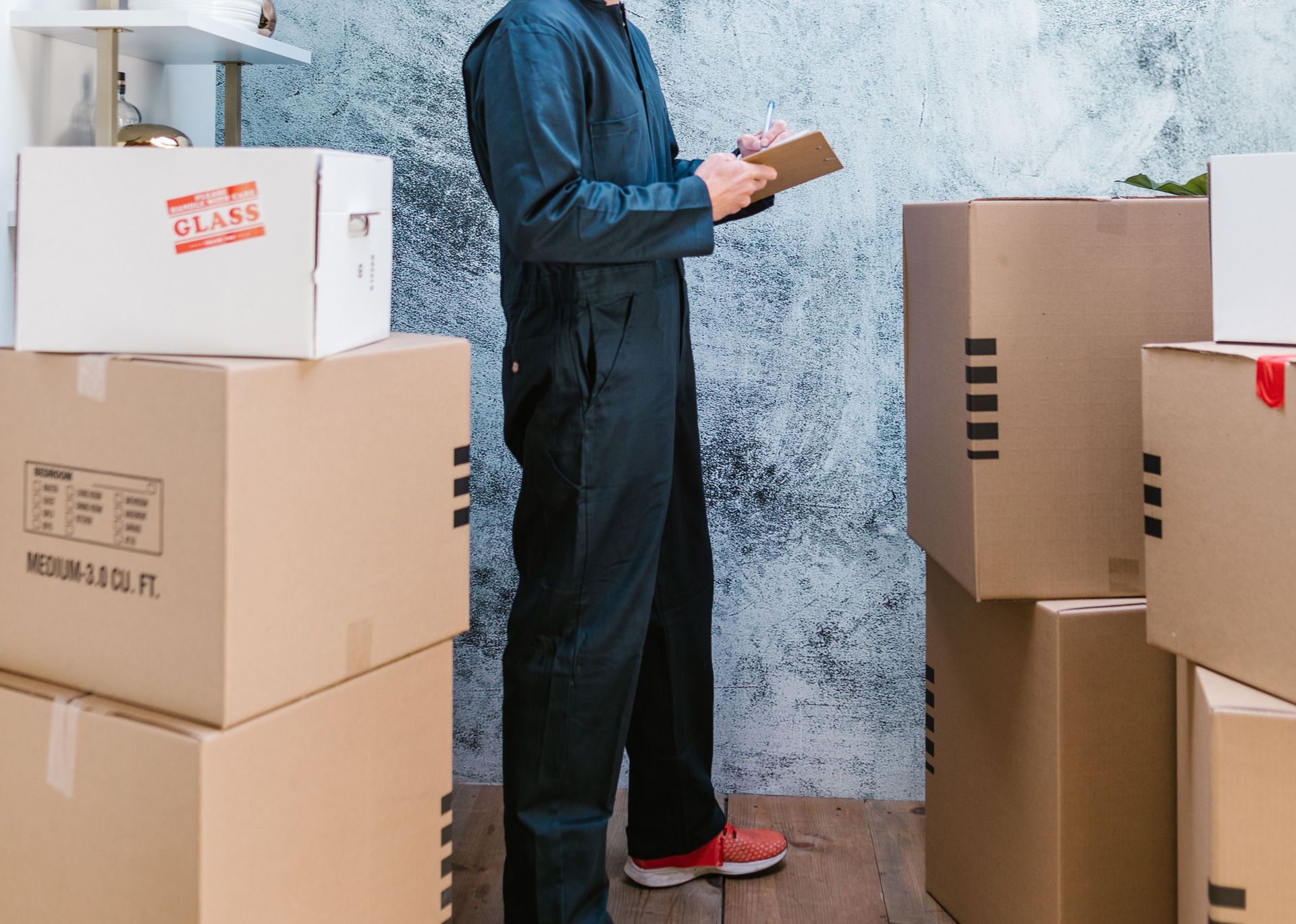 A mover in coveralls with bandana checks packages in a warehouse.